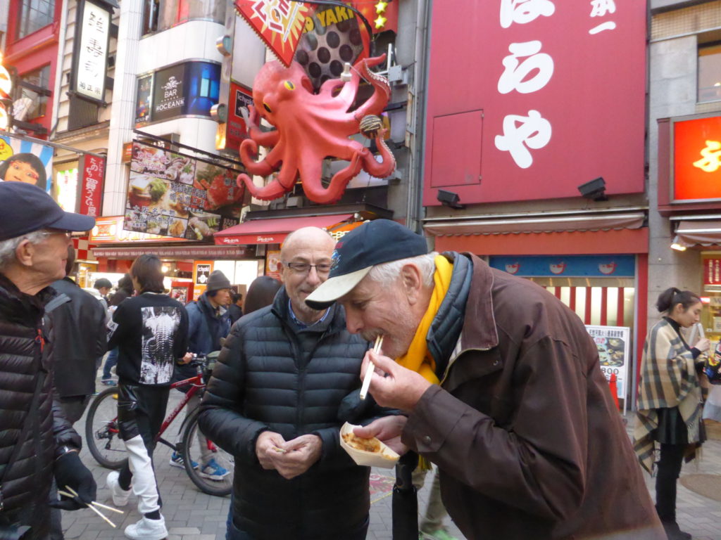 Western people eating takoyaki, street food in Japan, Japanese food, at Dotonbori district of Osaka, by journey to the east